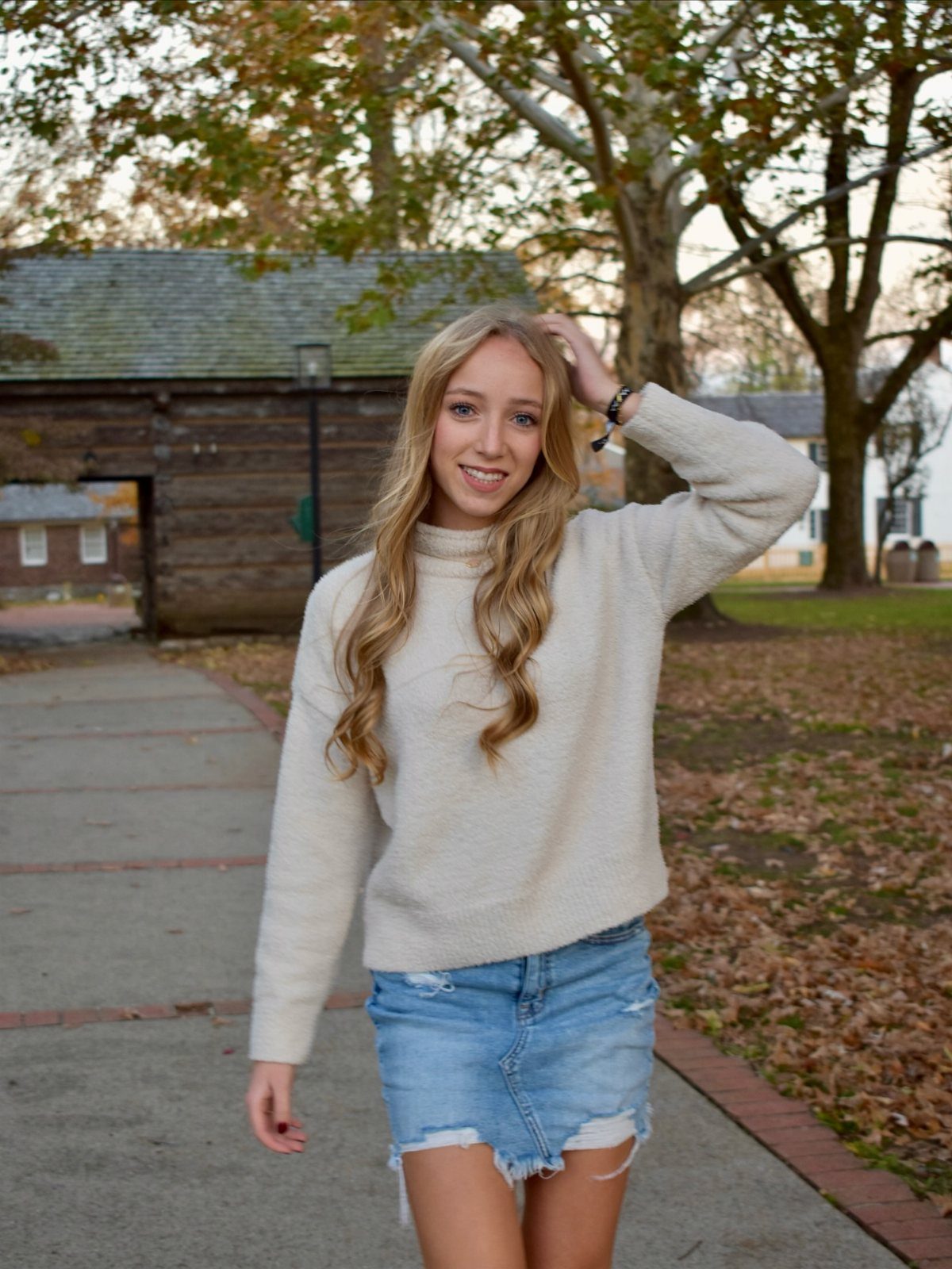 Young woman in a cream sweater and denim skirt posing in autumn setting