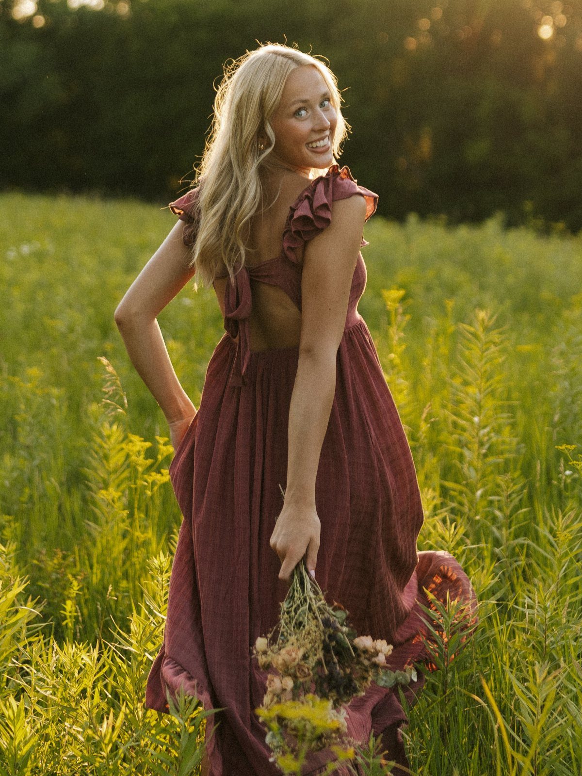 Blonde woman in a long maroon ruffled dress standing in a wildflower field