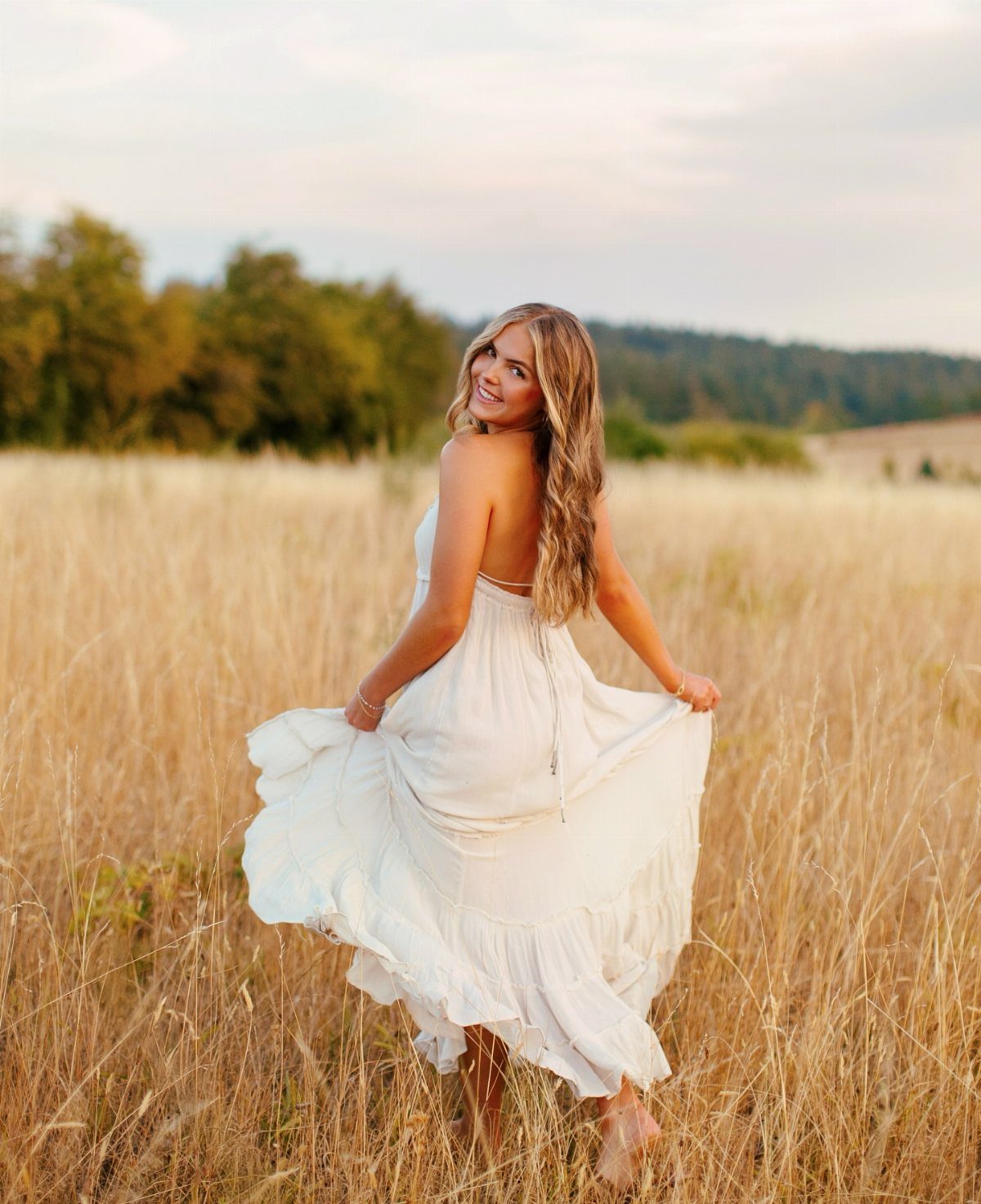 Young woman in a flowing white dress posing in a golden grass field