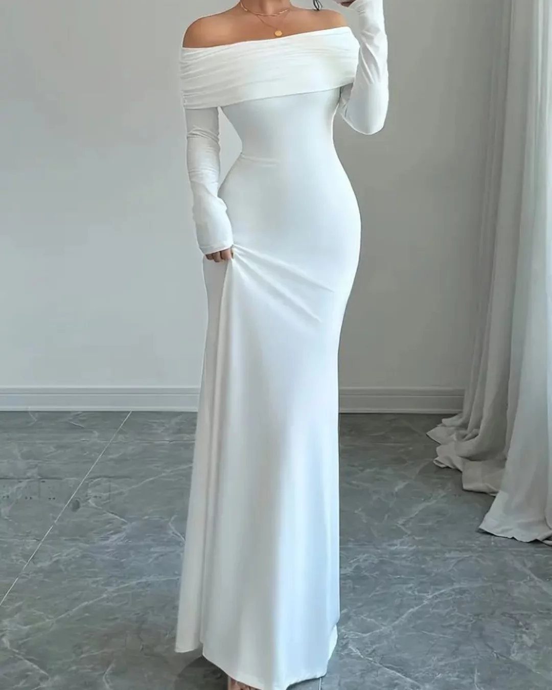 Woman wearing a long, form-fitting white off-the-shoulder dress on a marble floor