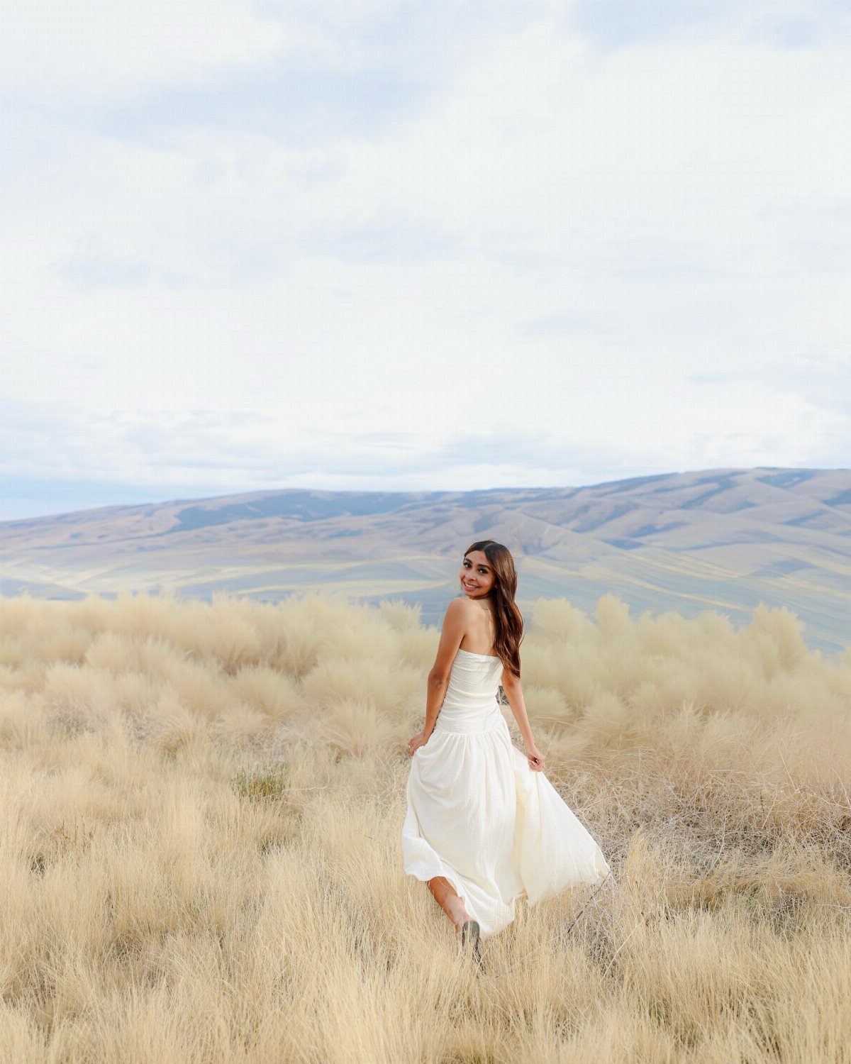 Young woman in a strapless white midi dress posing in a golden grass field.