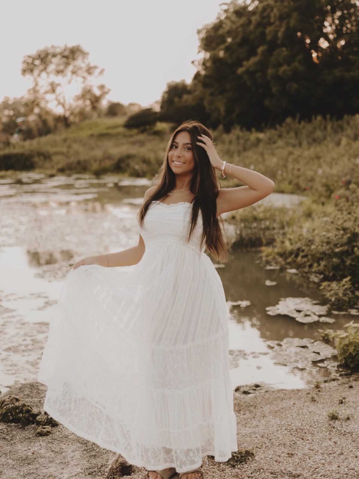 Young woman in a white strapless eyelet maxi dress posing by a pond