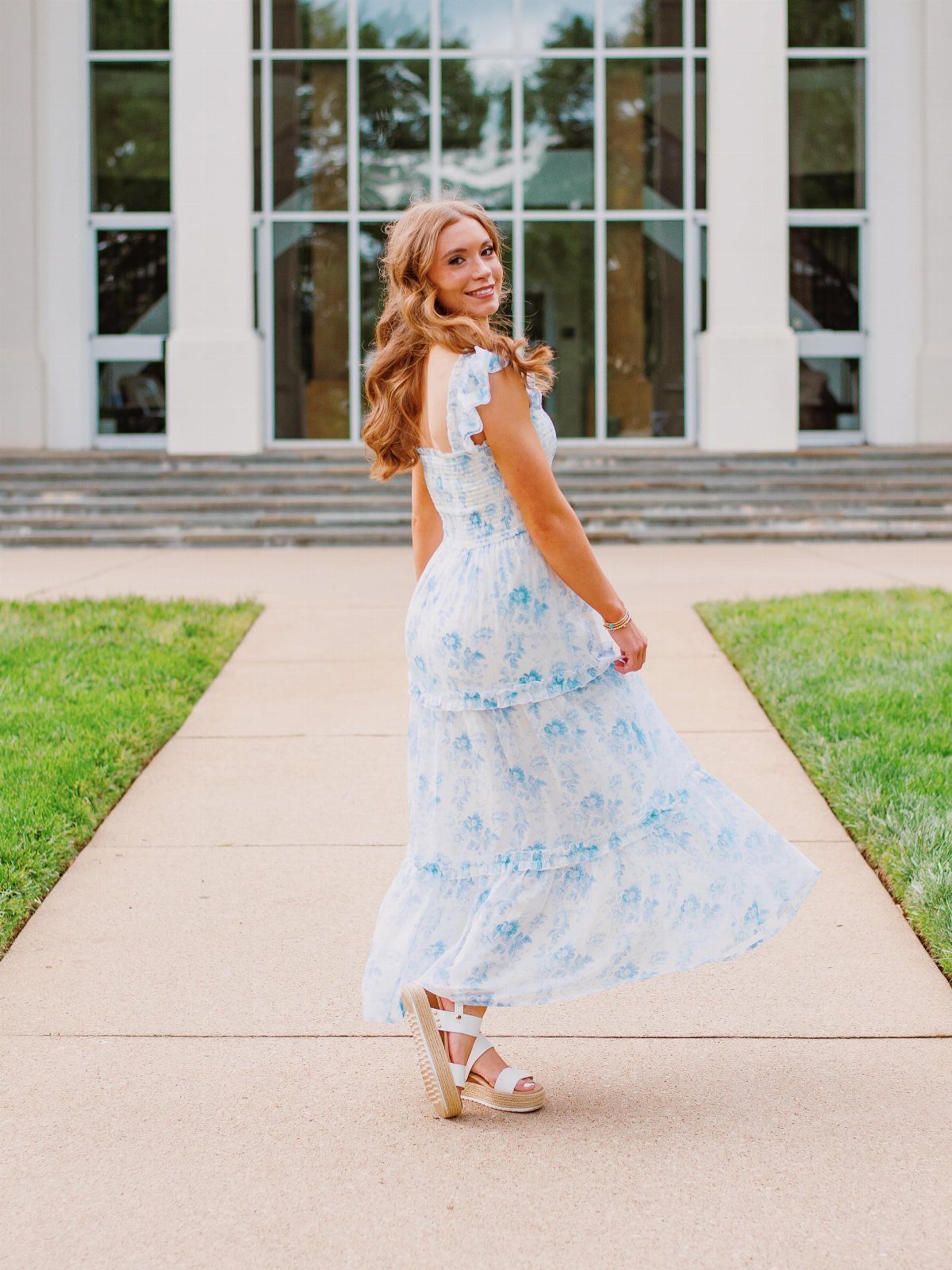 Young woman in a white and blue floral midi dress posing outdoors.