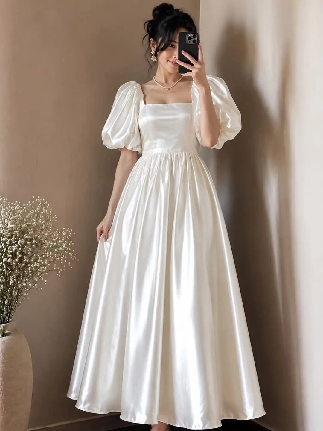 Woman in a white satin puff sleeve dress taking a mirror selfie indoors.