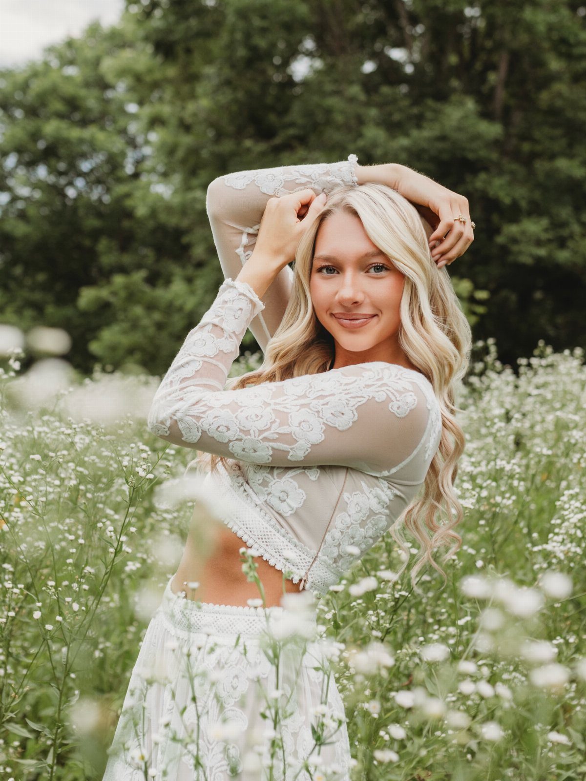 Young woman in white lace crop top and skirt posing in wildflower field