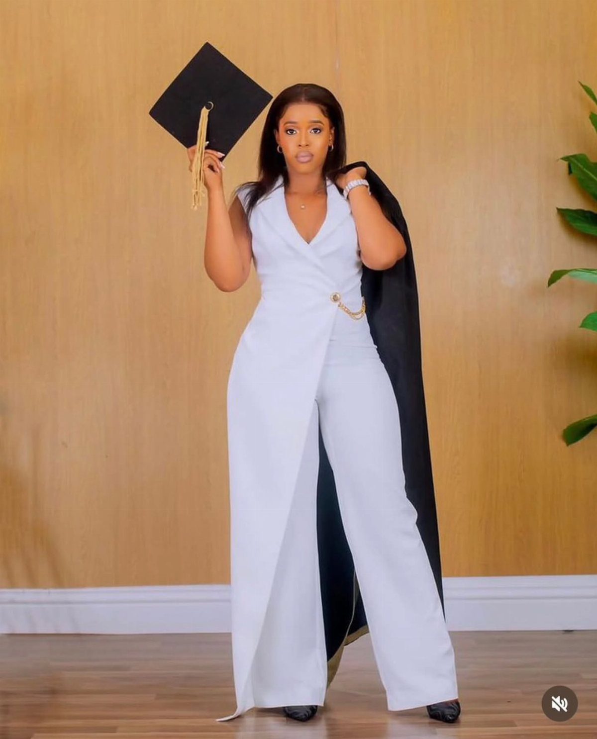 Woman in a white wide-leg jumpsuit holding a black graduation cap and gown.