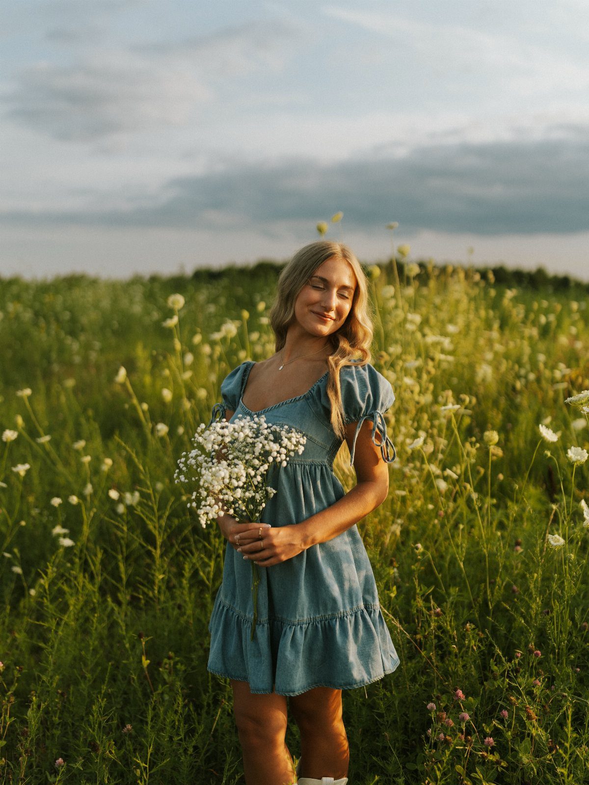 Young woman in a blue dress holding flowers in a sunny wildflower field