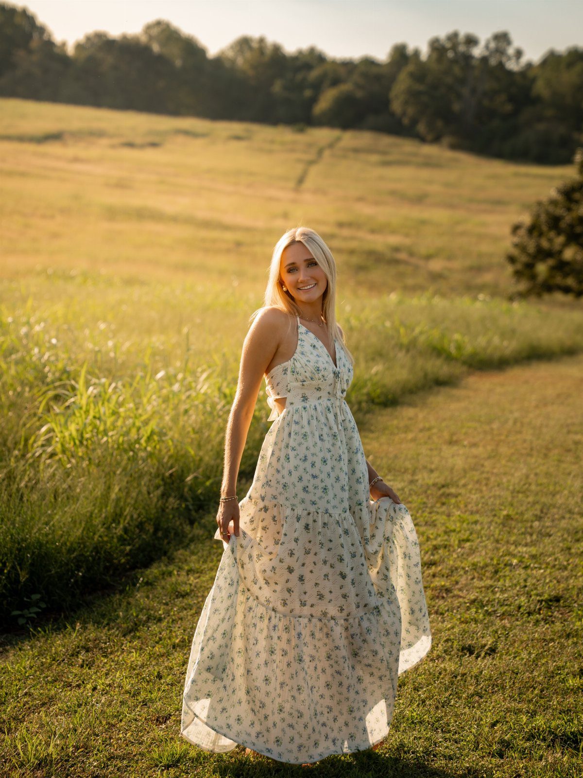 Blonde woman in a white floral maxi dress posing in a sunny field