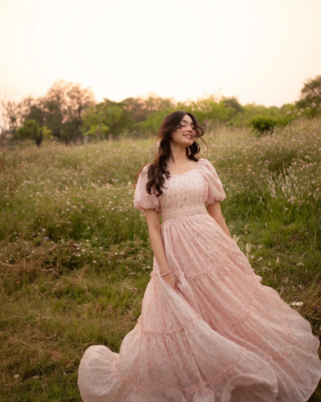 Young woman in a flowing pink tiered dress posing in a grassy field