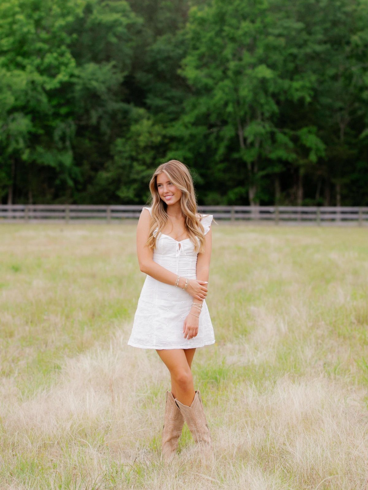 Young woman in a short white dress and tan boots posing in a field