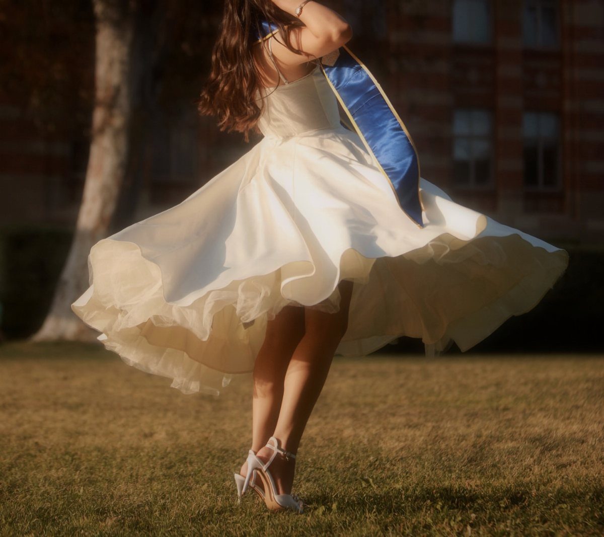Person in a voluminous white dress with a blue sash posing on grass