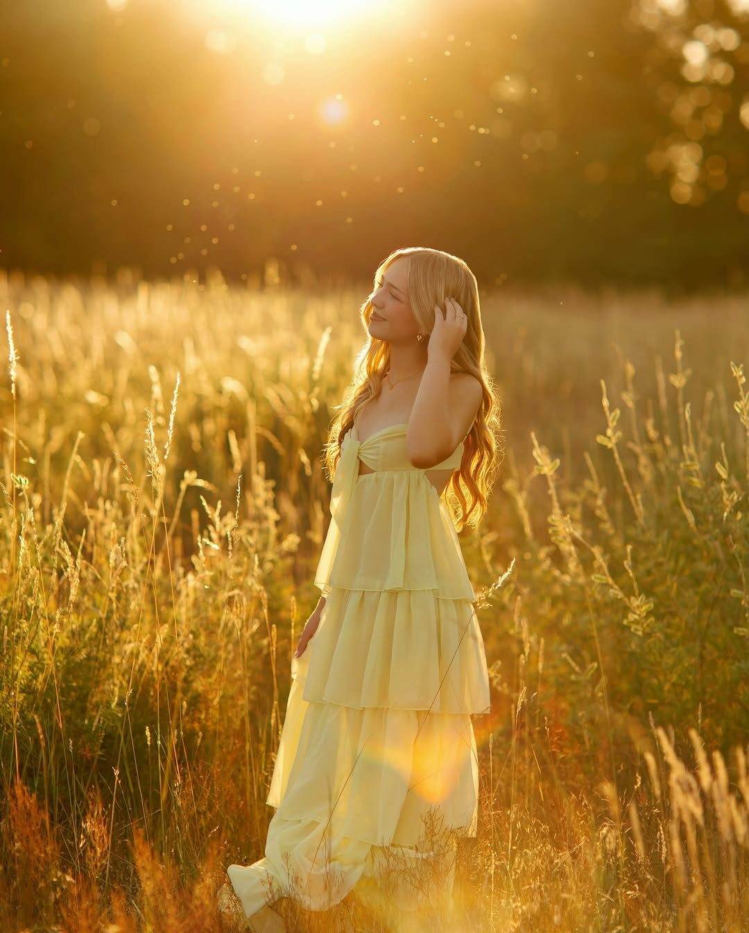 Young woman in a tiered yellow dress posing in a golden grassy field