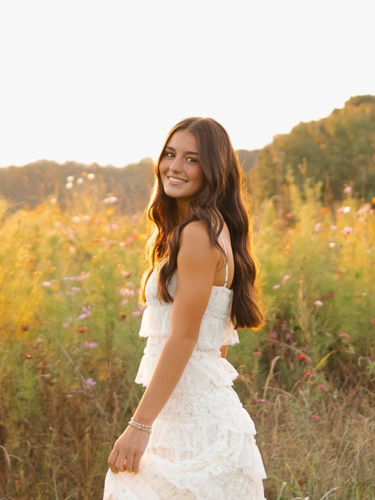 Young woman in a white tiered lace sundress smiling in a wildflower field