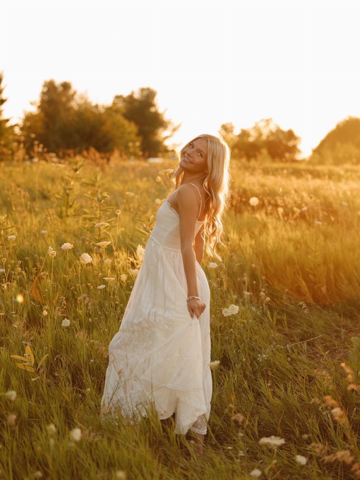 Young woman in a long white dress standing in a sunlit wildflower field