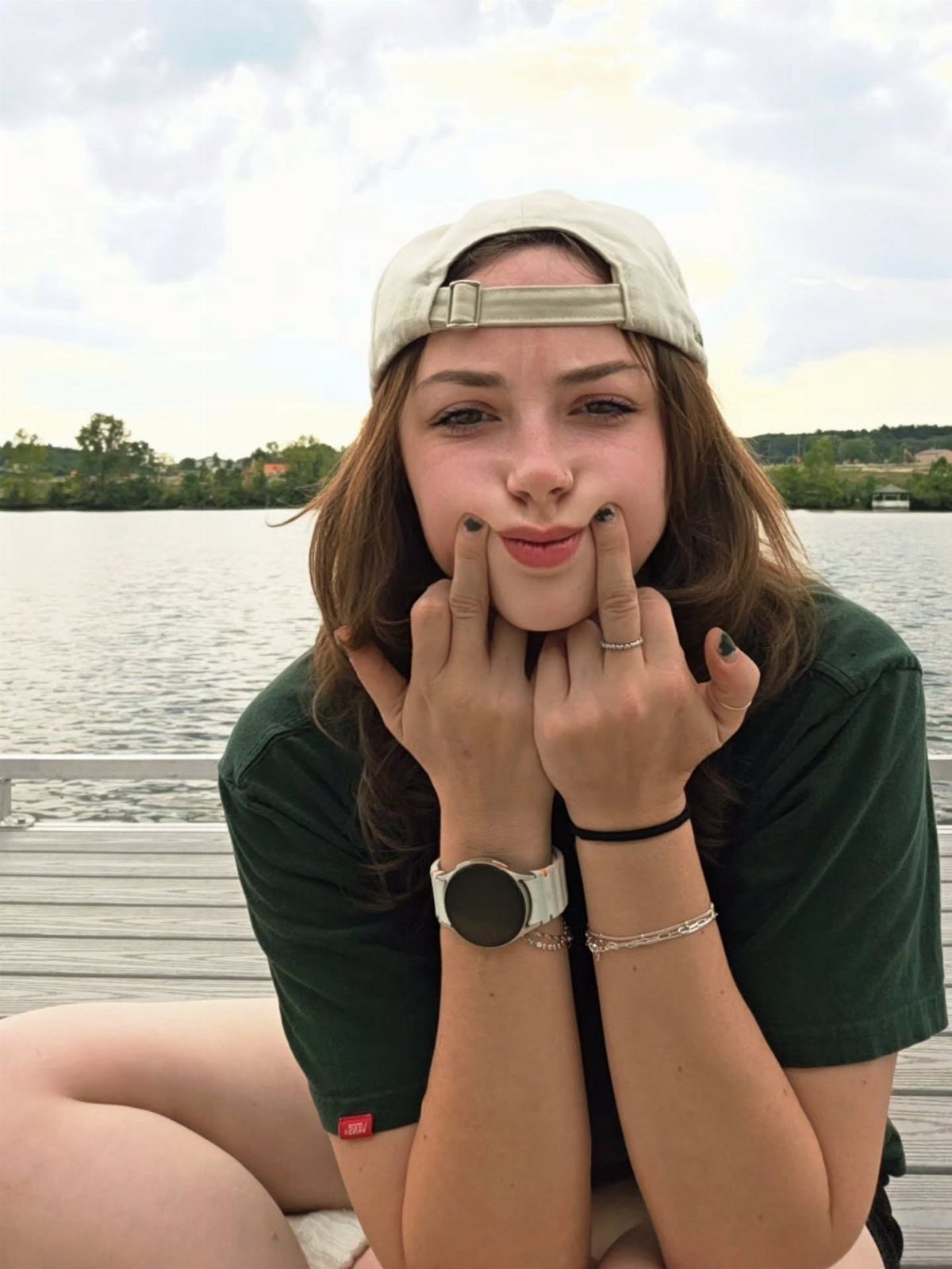 Young woman in a green t-shirt and backwards cap posing by a lake.