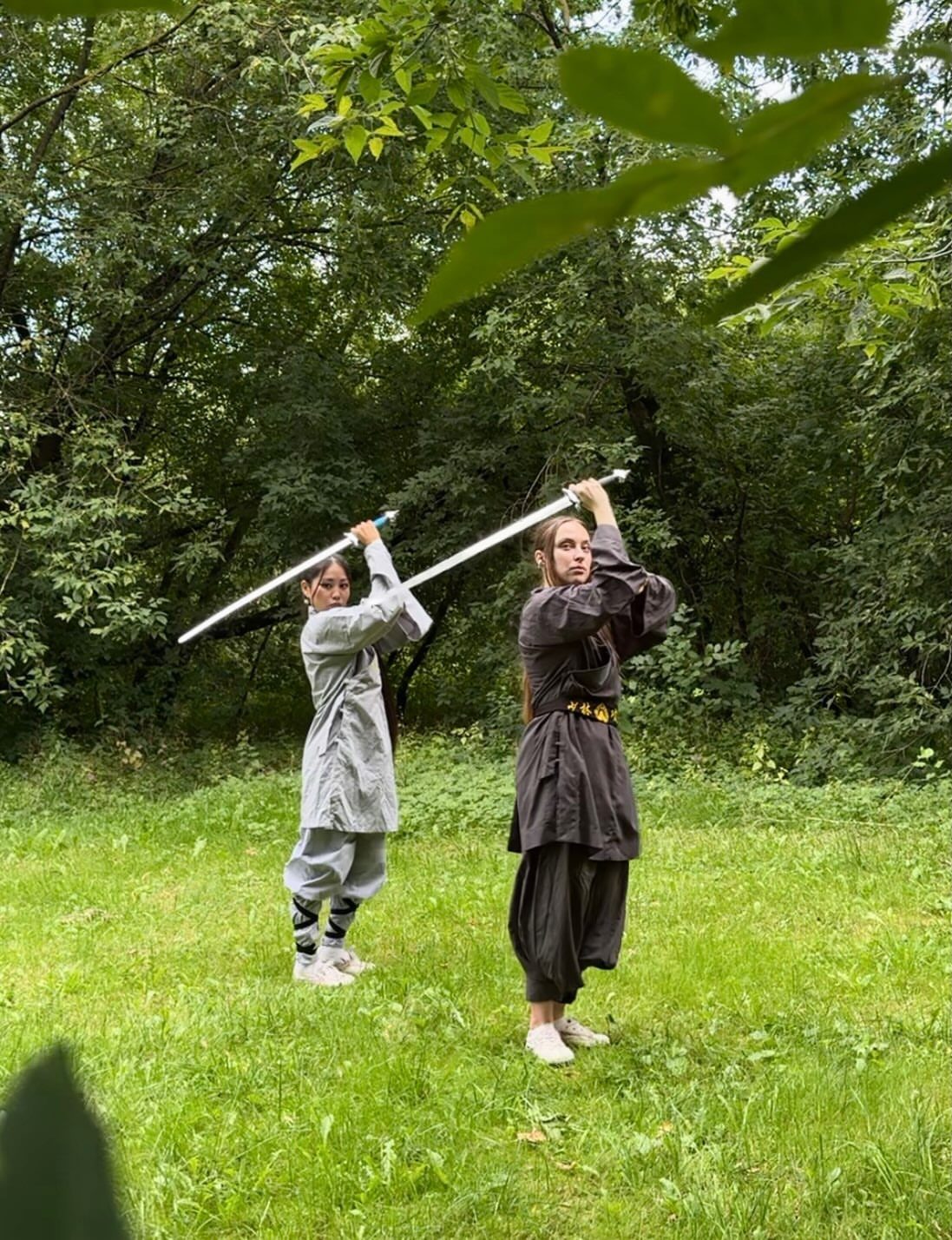 Two young women posing with swords in a forest for funny senior pictures.