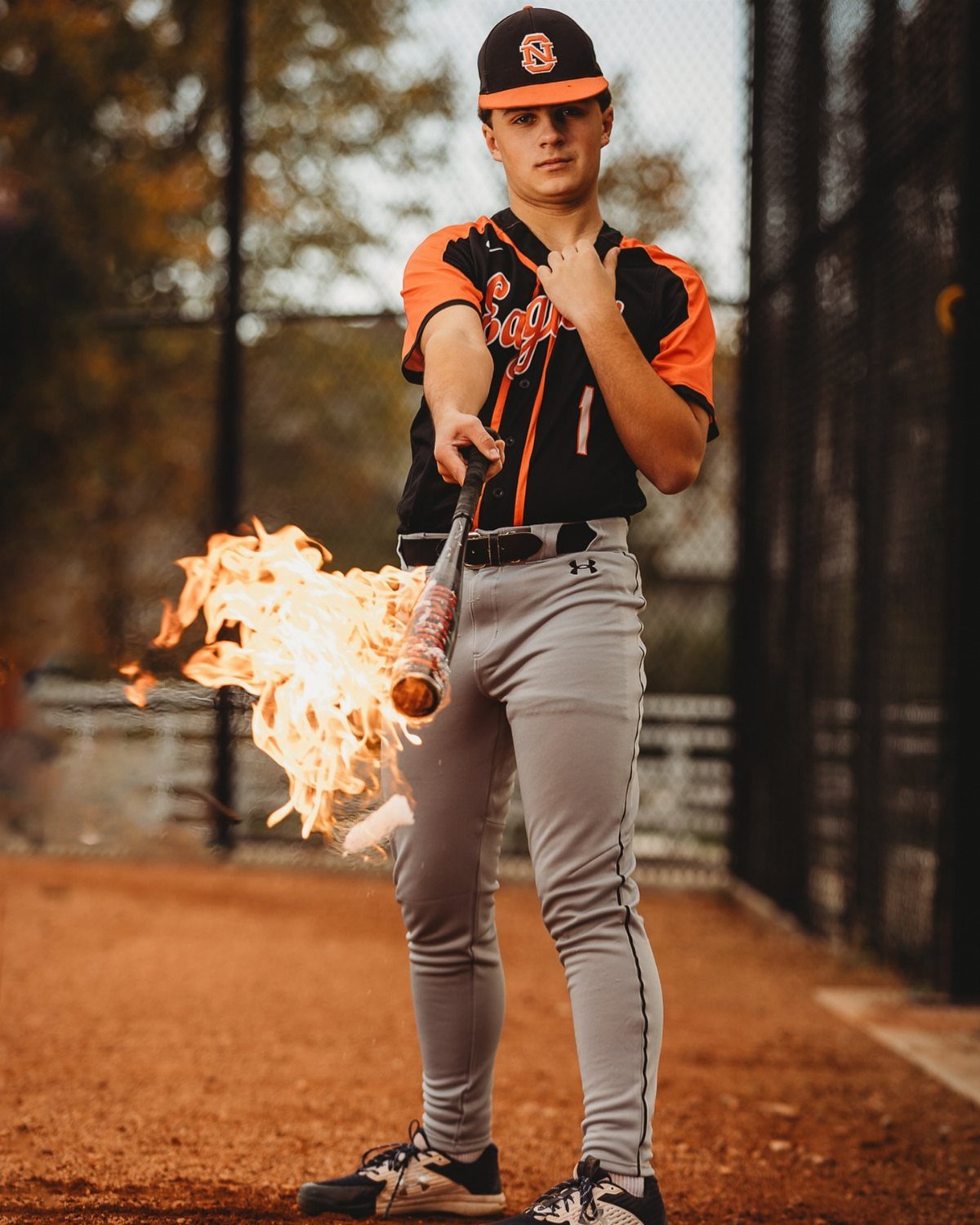 Baseball player in uniform holding a baseball bat with bright orange flames.