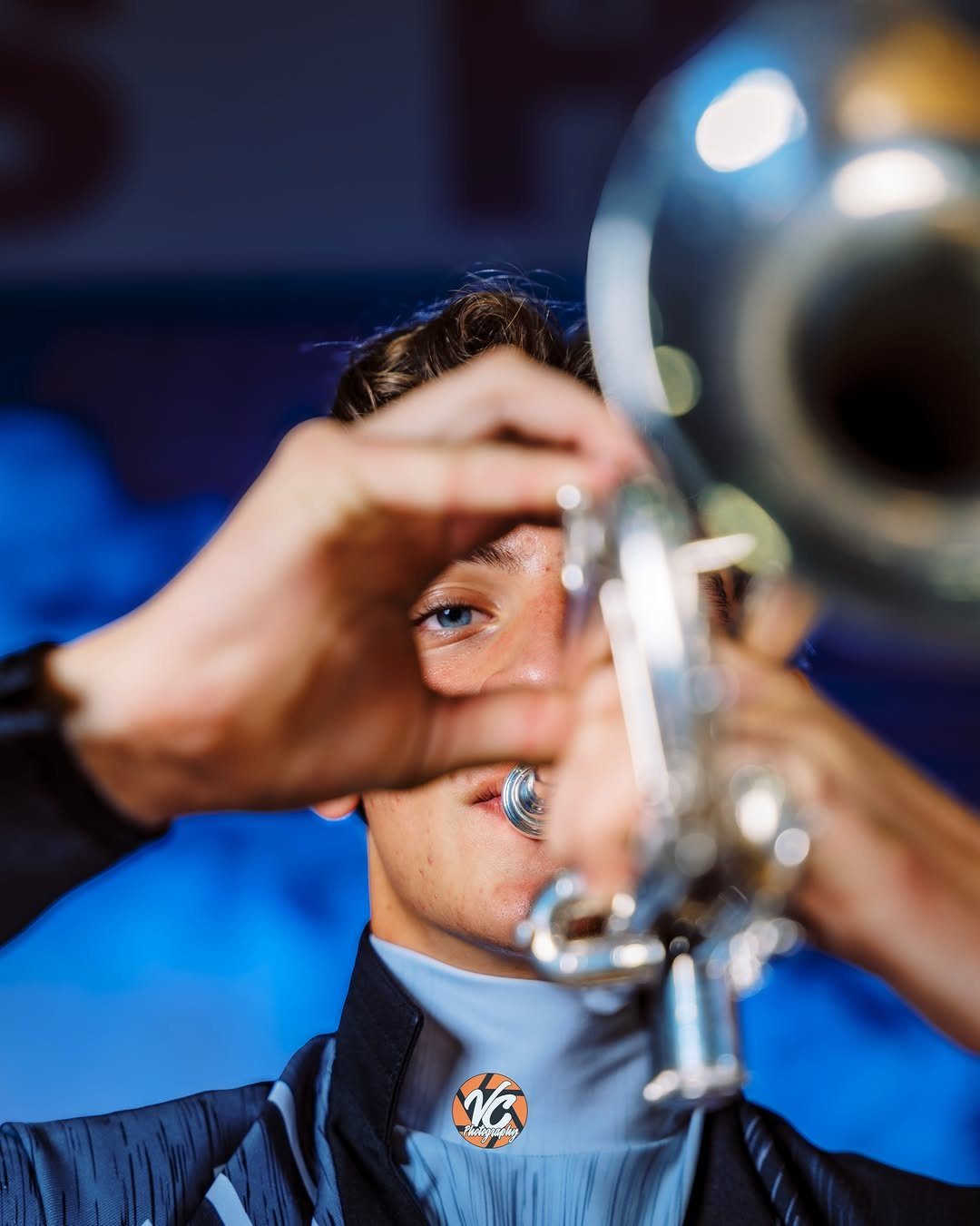 Young man peeking through a silver brass instrument in a creative portrait.