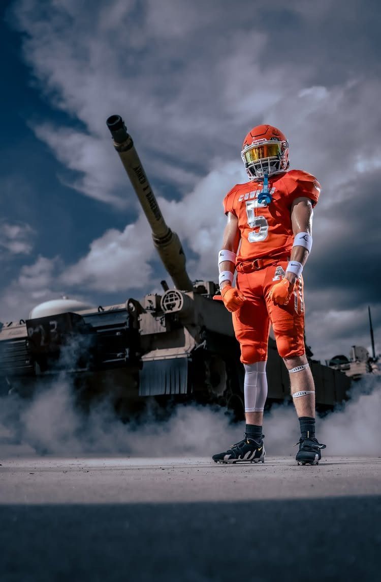 Football player in orange uniform posing in front of a military tank with smoke.