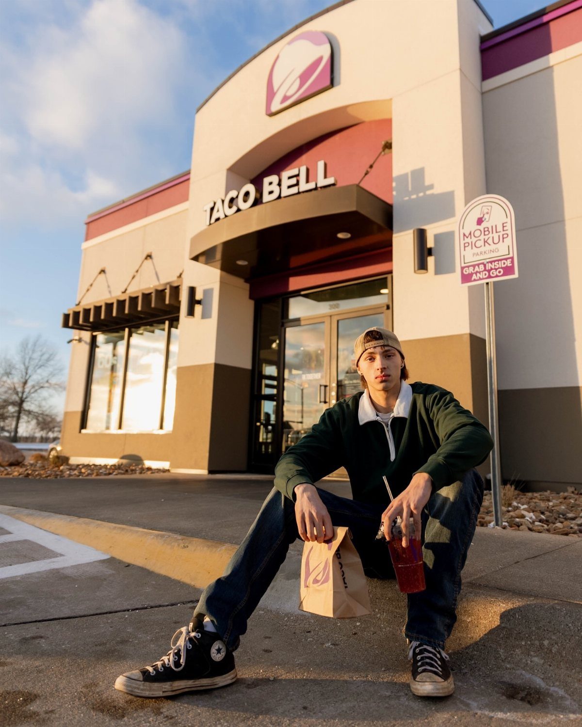 Young man sitting in front of a Taco Bell with fast food