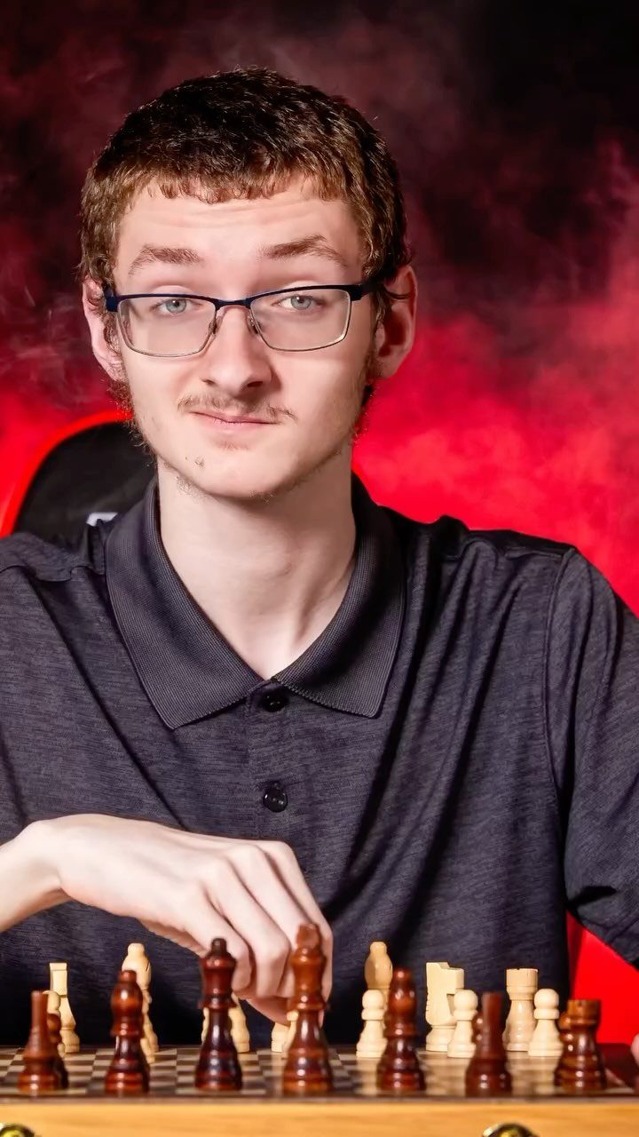 Young man with glasses posing with a chessboard against a red studio background