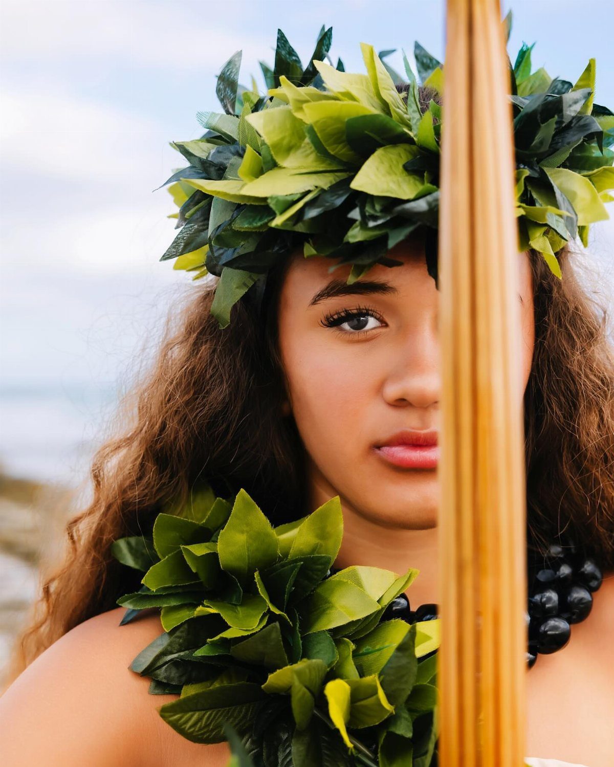 Young woman wearing traditional green leaf crown and lei at a beach