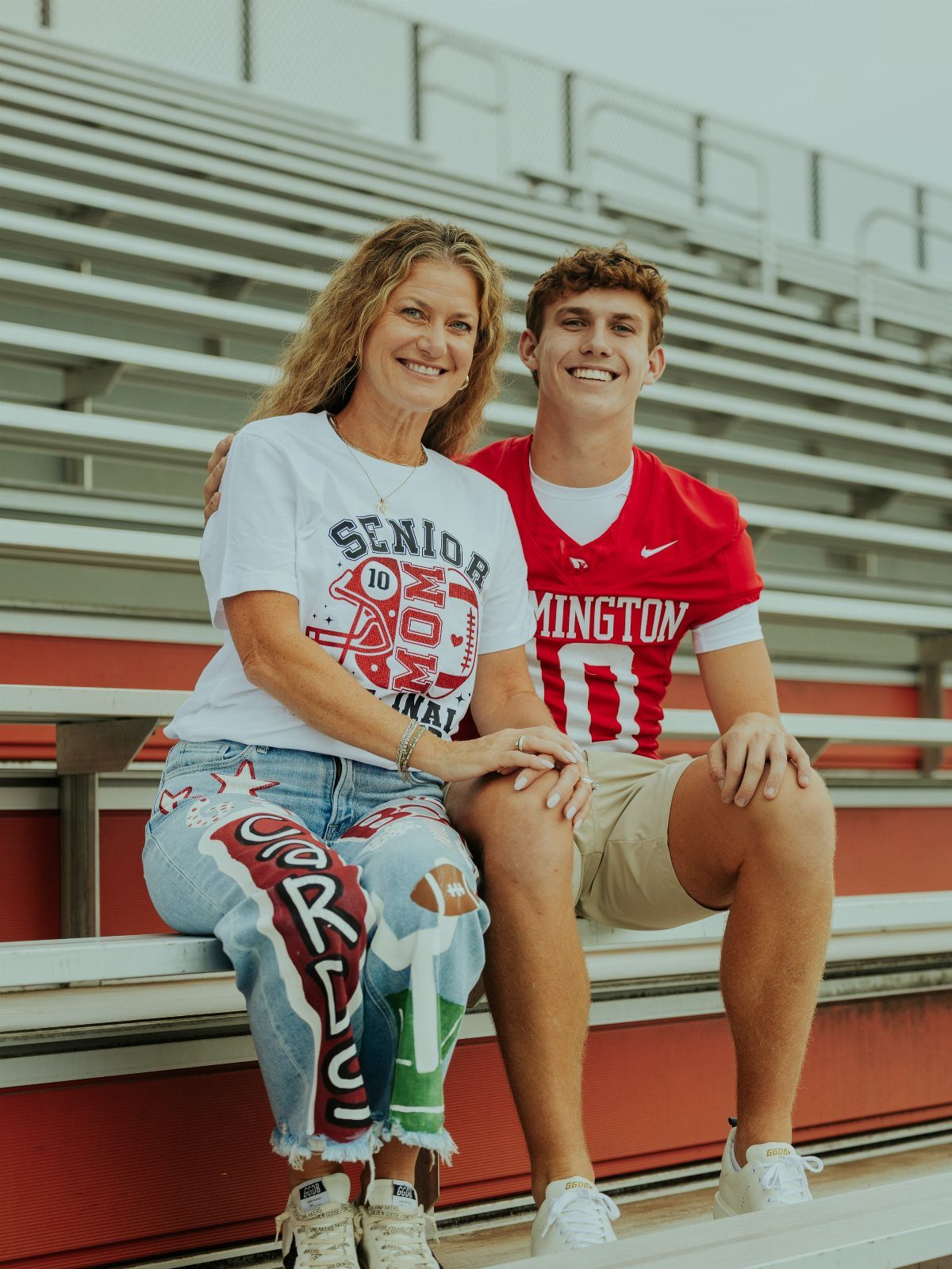 Woman and young man smiling while sitting together on outdoor stadium bleachers.
