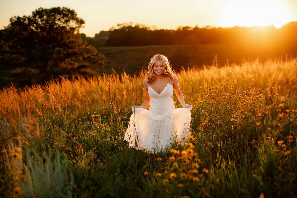 Smiling young woman in a white dress laughing in a golden sunset field