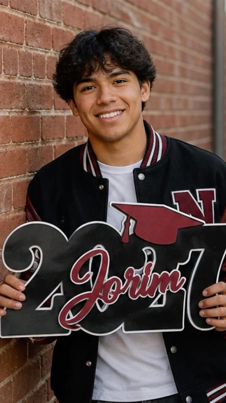 Smiling young man in a letterman jacket holding a personalized 2017 graduation sign.