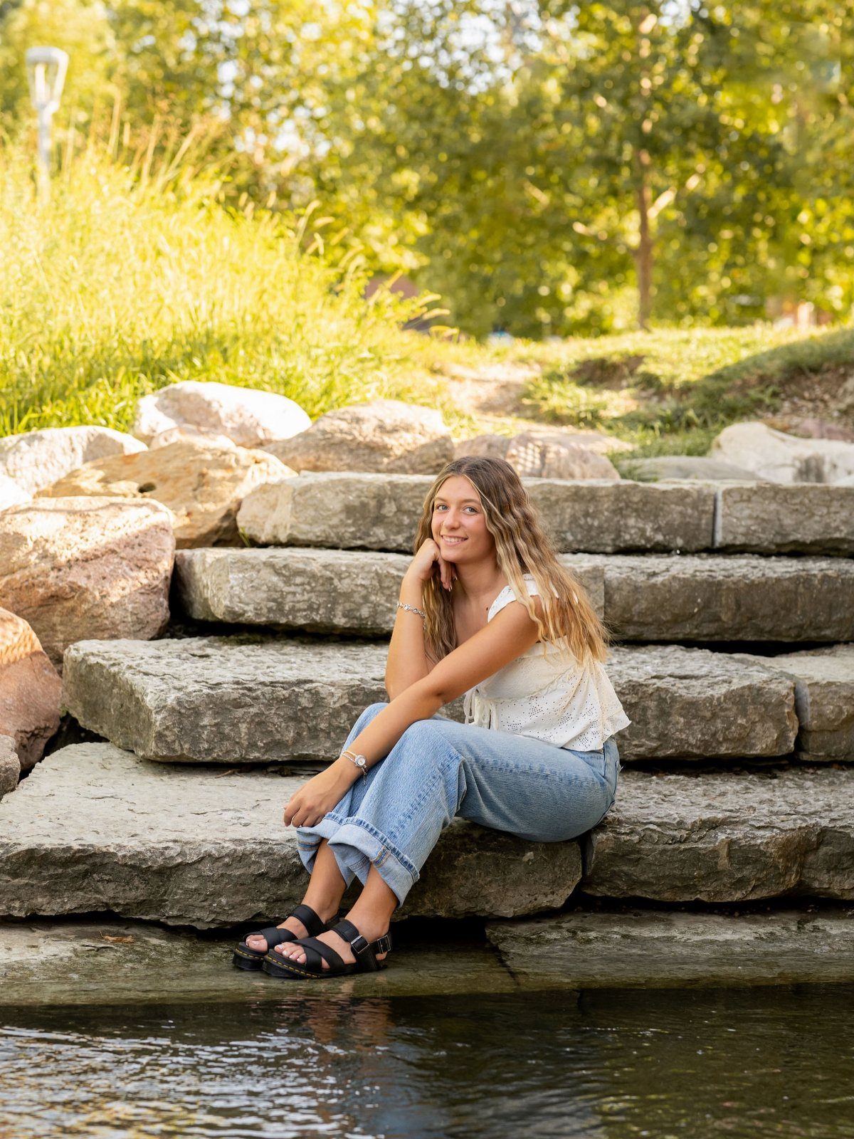 Young woman in white top and jeans sitting on stone steps by water