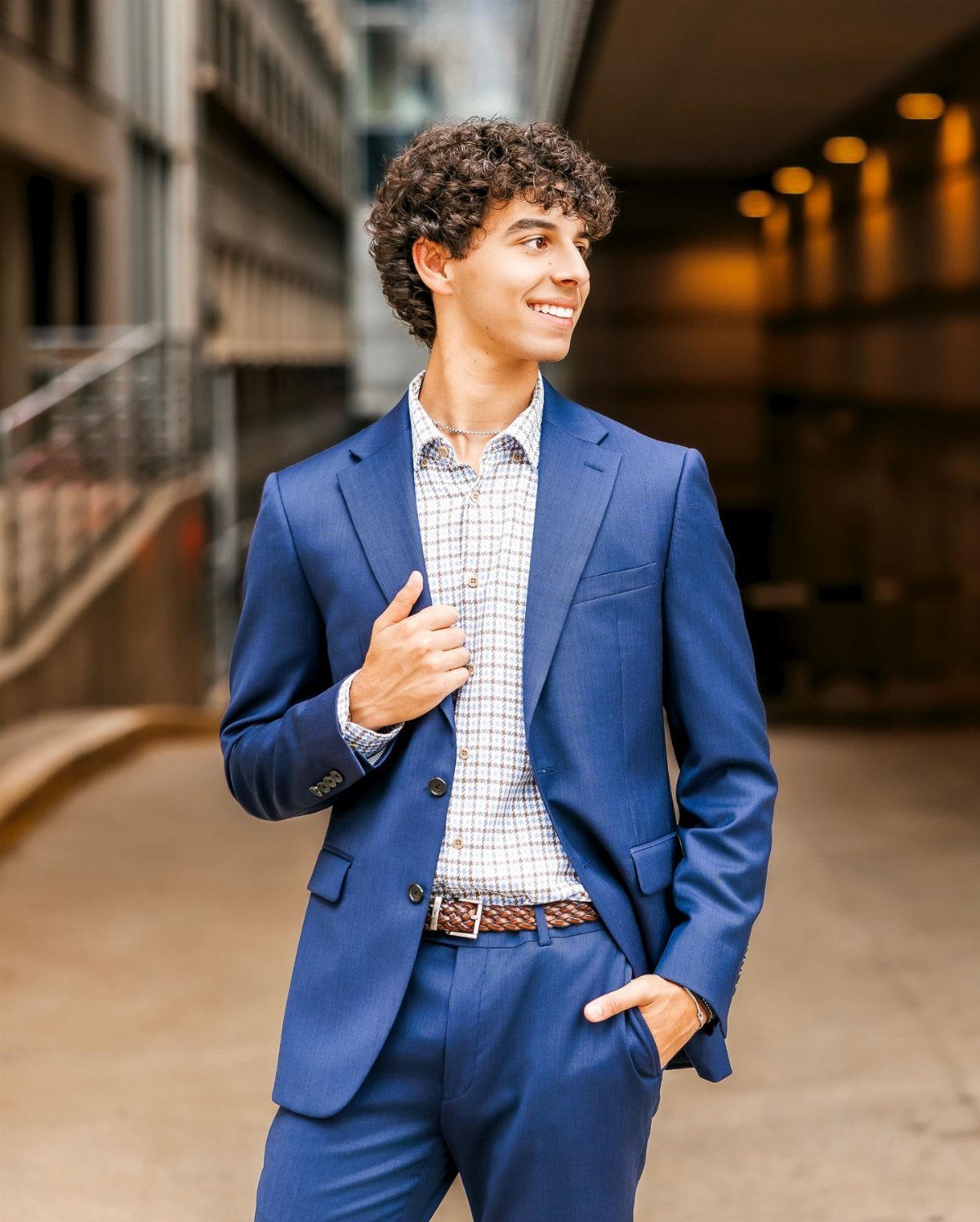 Young man in a blue suit smiling in an urban outdoor setting.