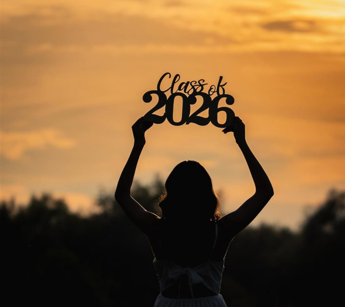 Silhouette of a graduate holding a Class of 2026 sign against a sunset.