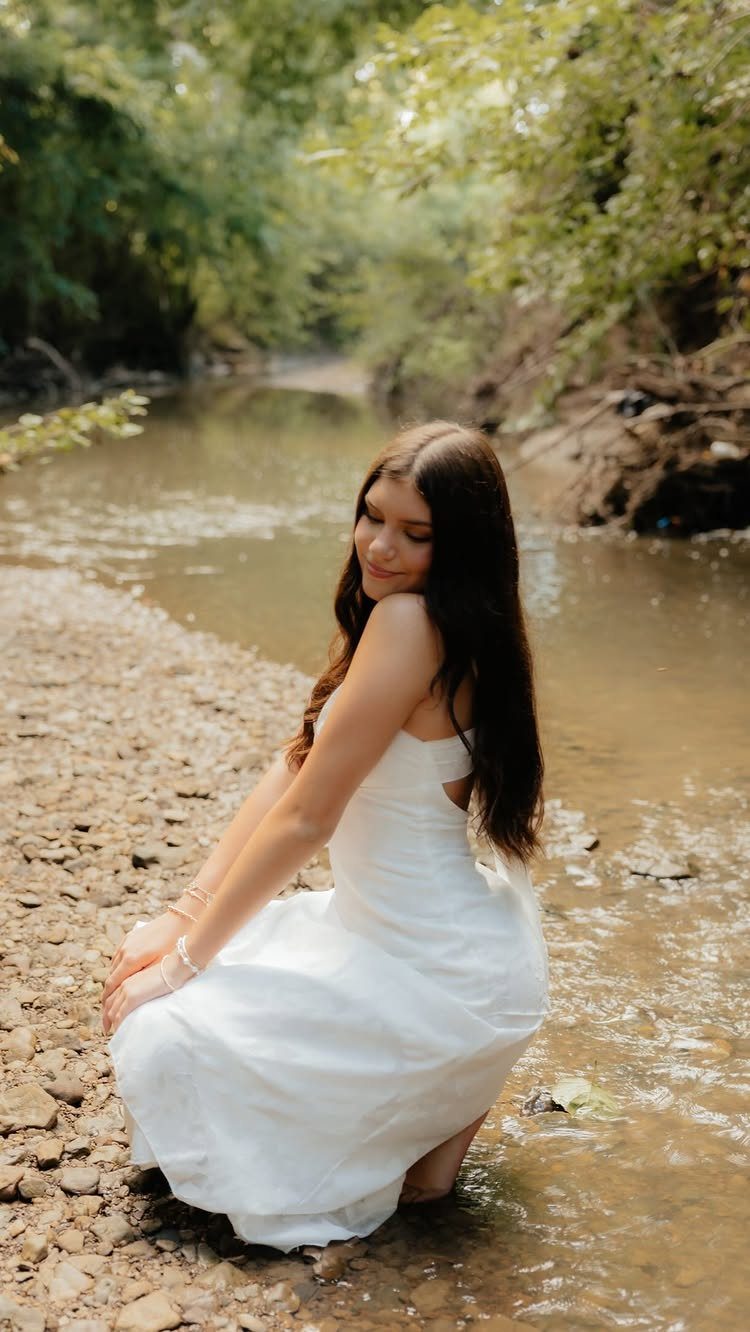 Young woman in a white dress sitting on a rocky riverbank in warm light