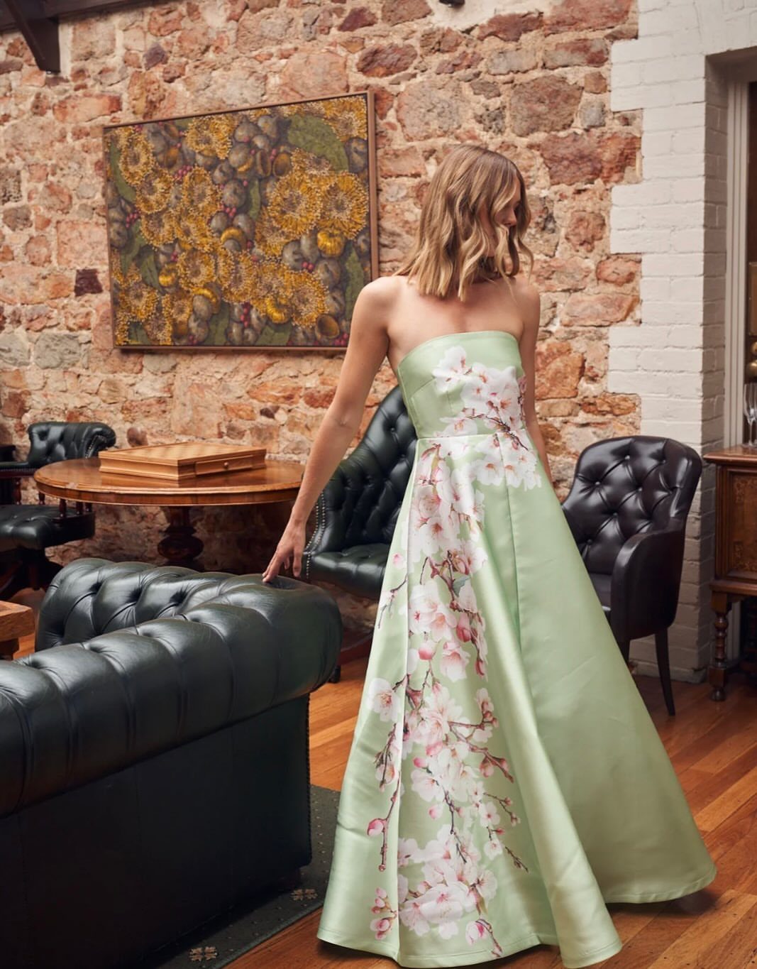 Woman wearing a light green strapless gown with pink floral prints in a room.