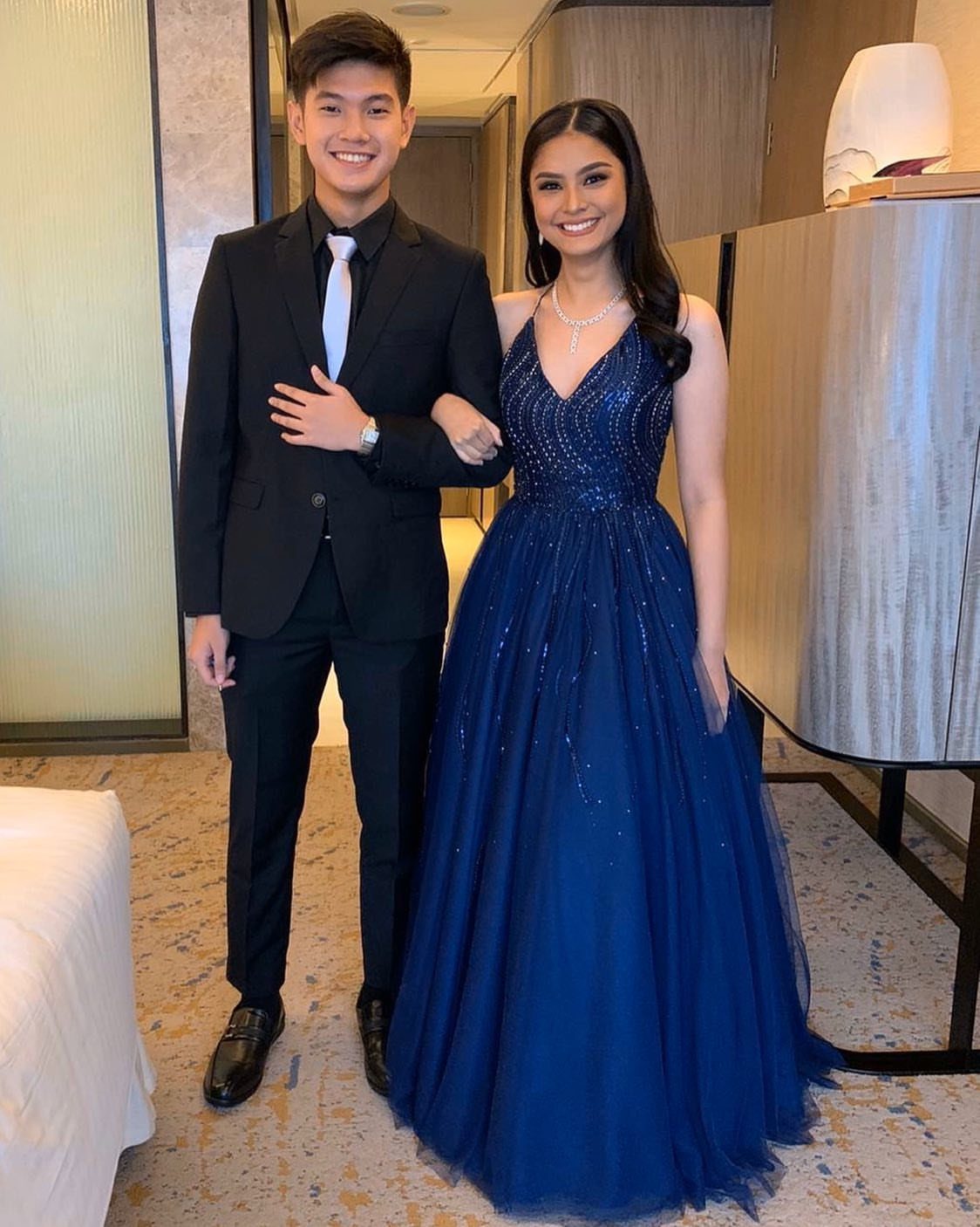Young couple posing, woman wearing a navy blue sequined floor-length prom gown.