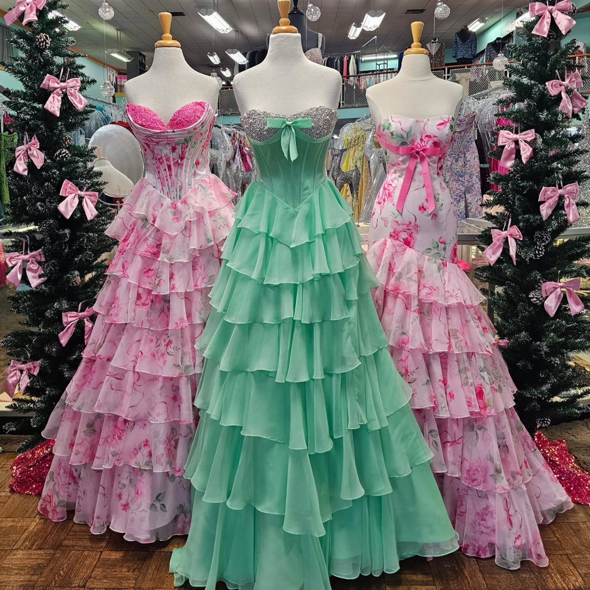 Three tiered ruffled prom dresses in mint green and floral pink on mannequins.