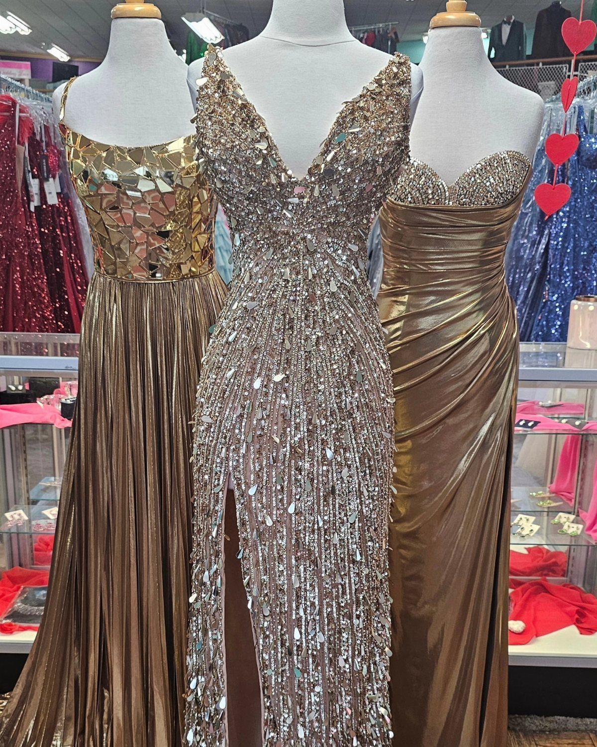 Three formal prom gowns on mannequins, featuring a silver sequined dress in center.