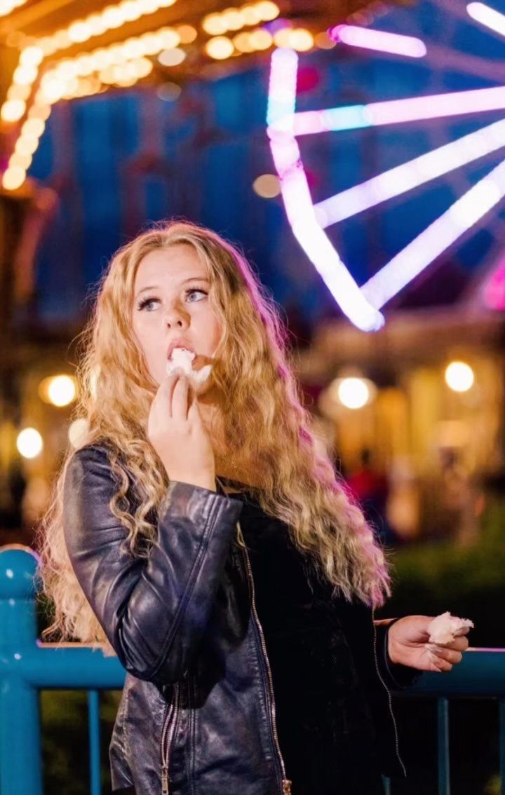 Young woman eating cotton candy with a glowing Ferris wheel in the background