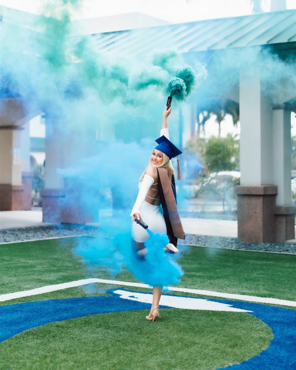Graduating woman in cap and gown holding a canister emitting bright blue smoke.