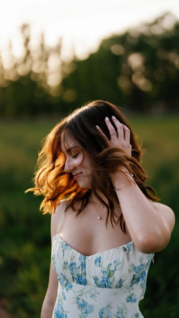 Young woman in floral dress posing in a field during golden hour sunlight.