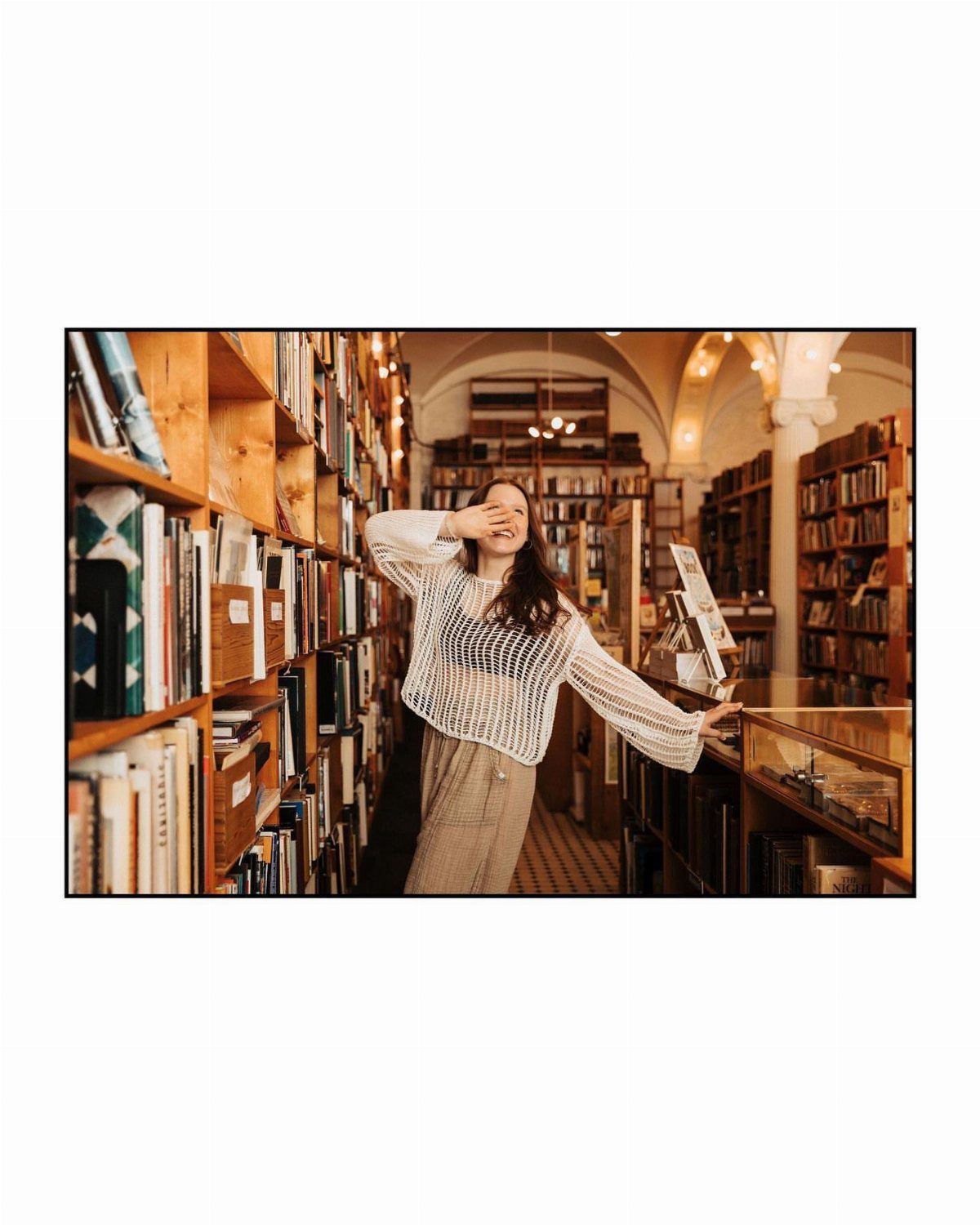Young woman posing between wooden bookshelves in a classic library setting