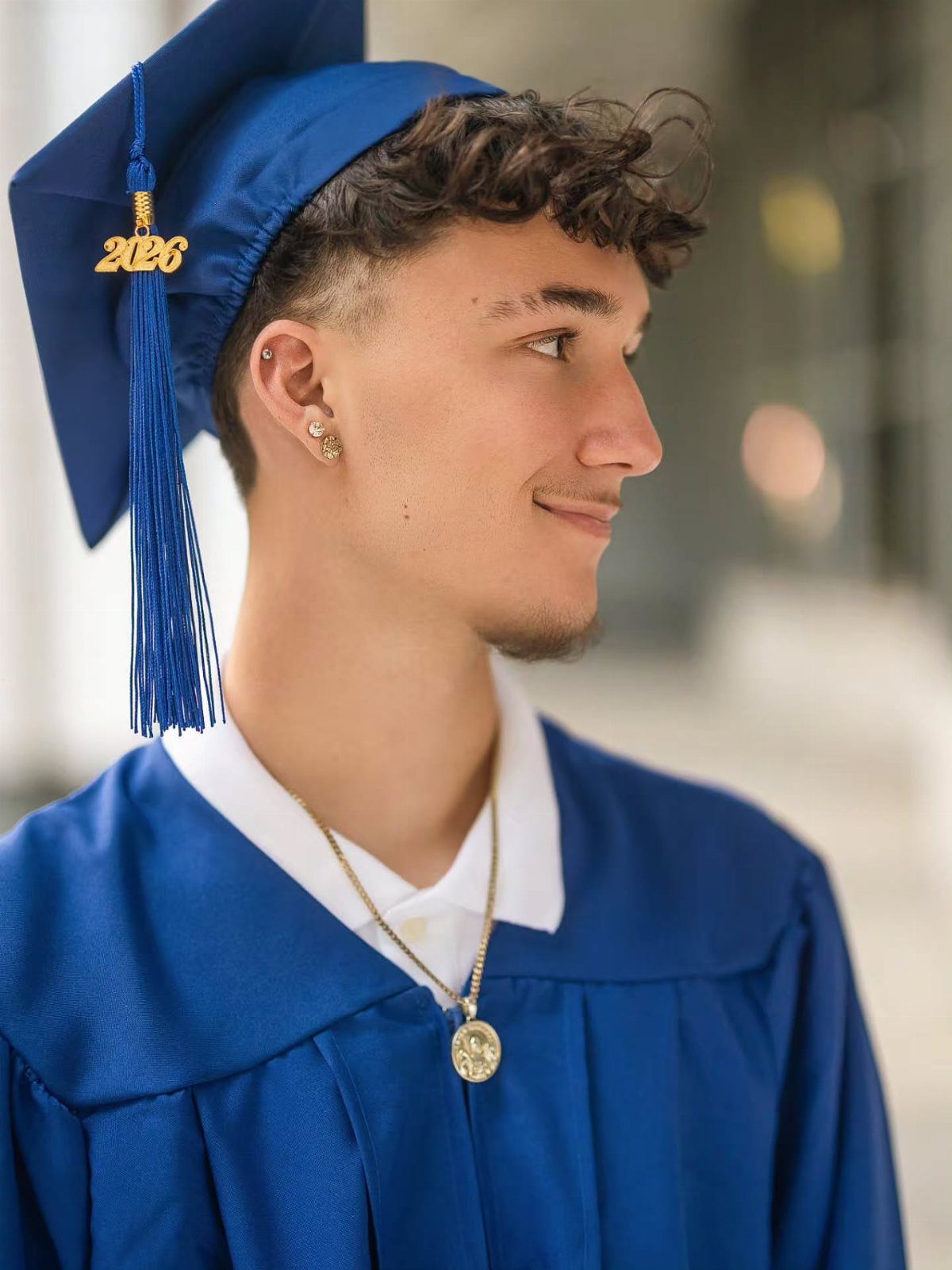 Young man in a royal blue graduation cap and gown smiling in profile.