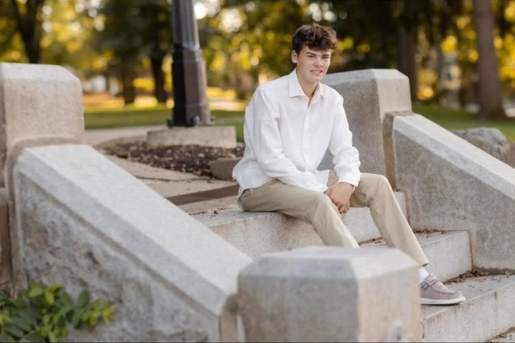 Young man in white shirt and khakis sitting on concrete outdoor steps smiling