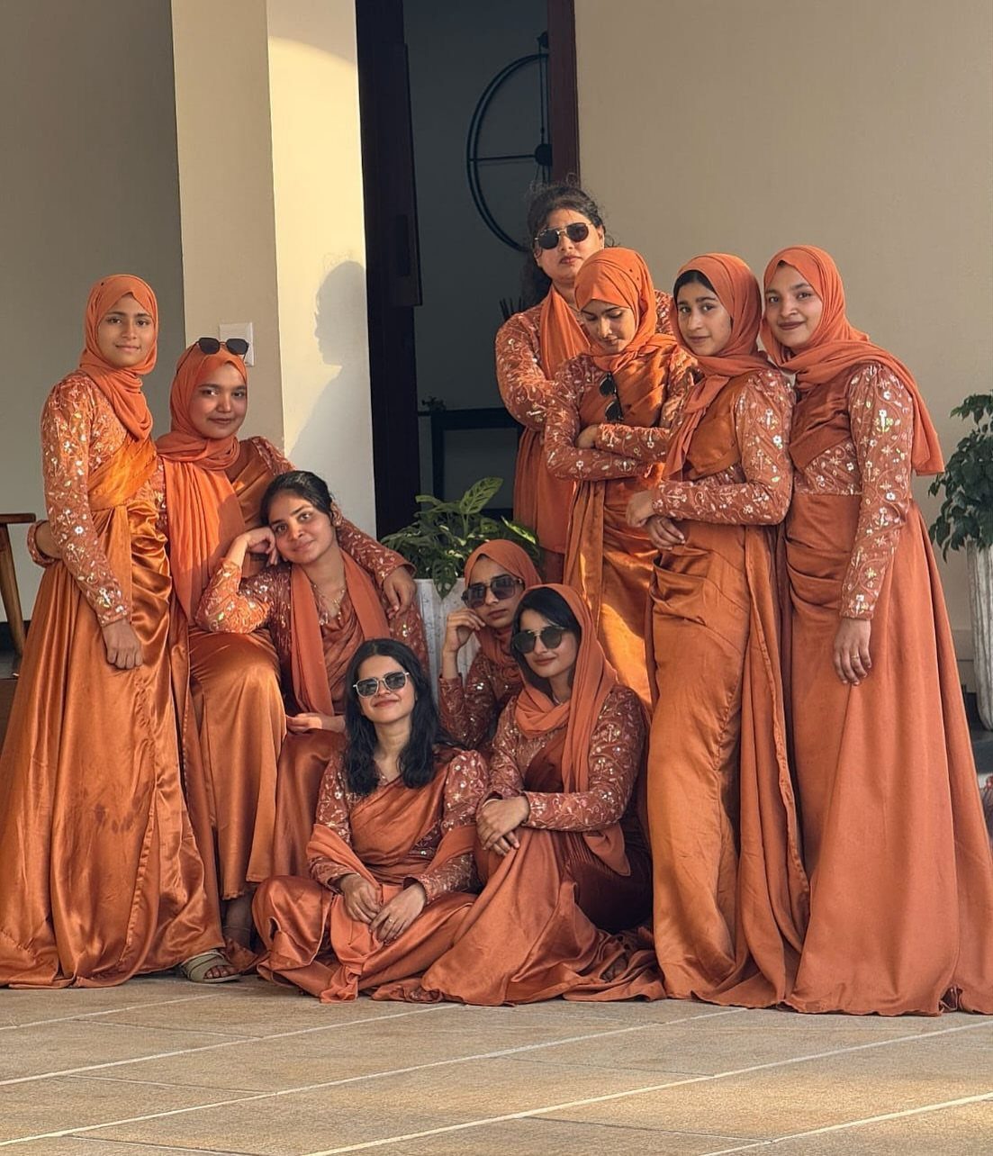 Women in matching burnt orange satin gowns and hijabs posing on a patio.