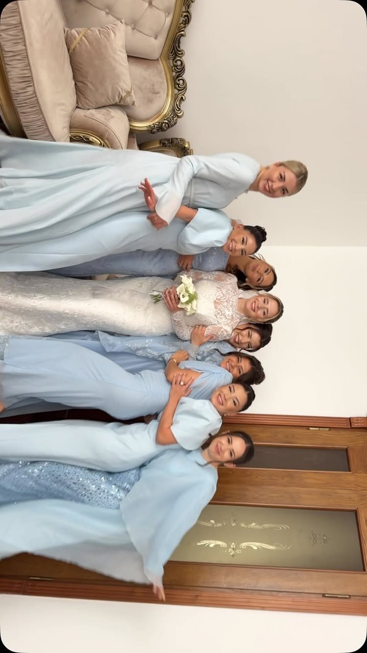 Bride in white lace gown surrounded by bridesmaids in light blue dresses.