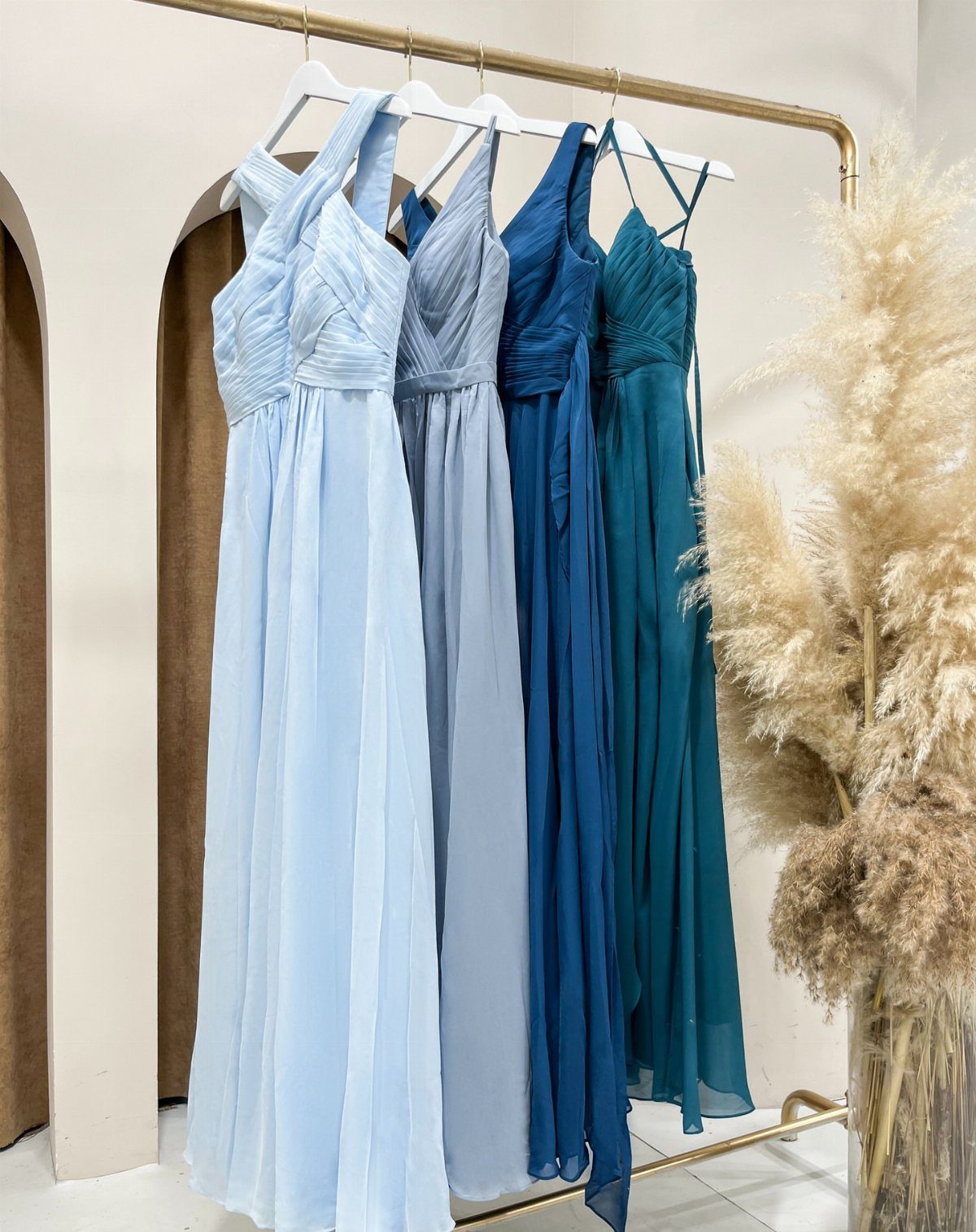 Four blue bridesmaid dresses in different shades and styles hanging on a gold rack.