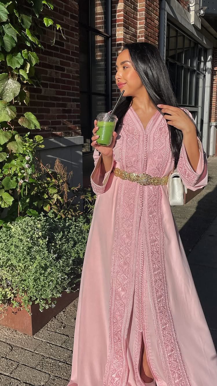 Woman in a long light pink embroidered dress with a gold belt outdoors.