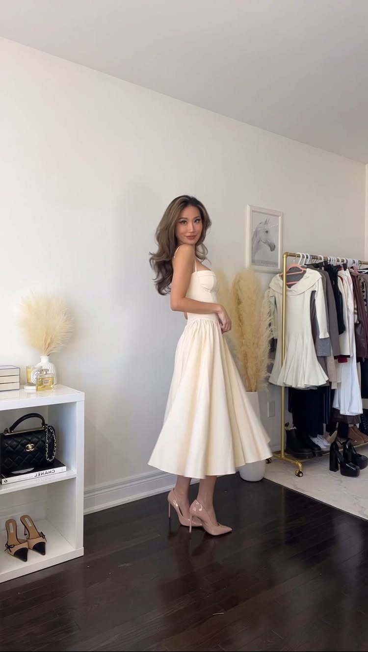 Woman wearing a cream-colored A-line midi dress and nude heels in a room.